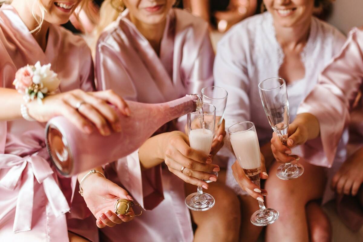 Young bridesmaids clinking with glasses of champagne in hotel room. Closeup photo of cheerful girls celebrating a bachelorette party. Females have toast with wine.