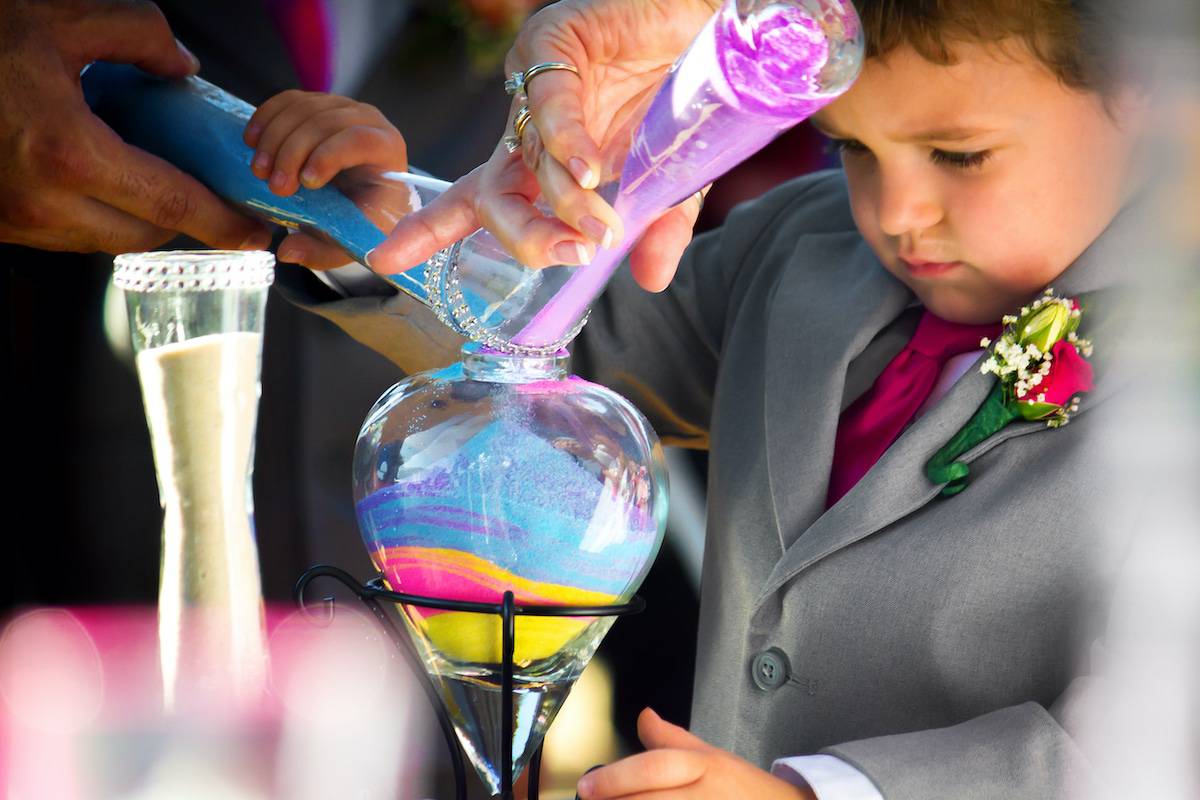 A ring bearer, who is the son of the bride, pours colored sand in the unity ceremony during a wedding.