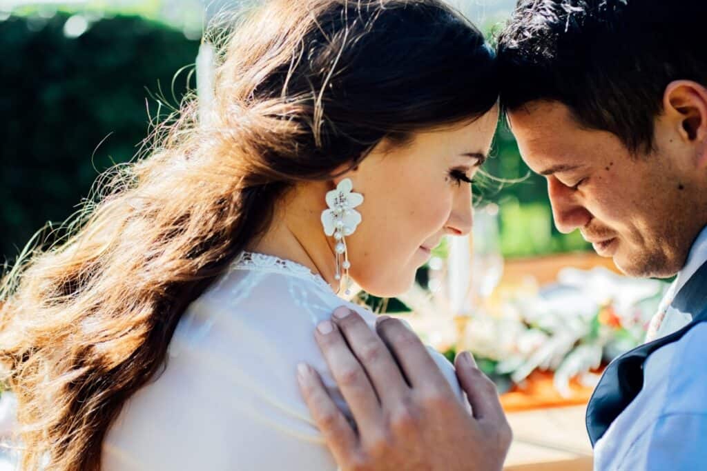 Wedding couple with head touching and eyes closed while at wedding dinner table outside.
