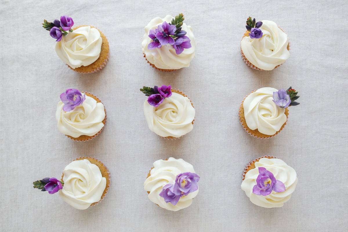 whipped cream frosting vanilla cupcakes with purple edible flowers