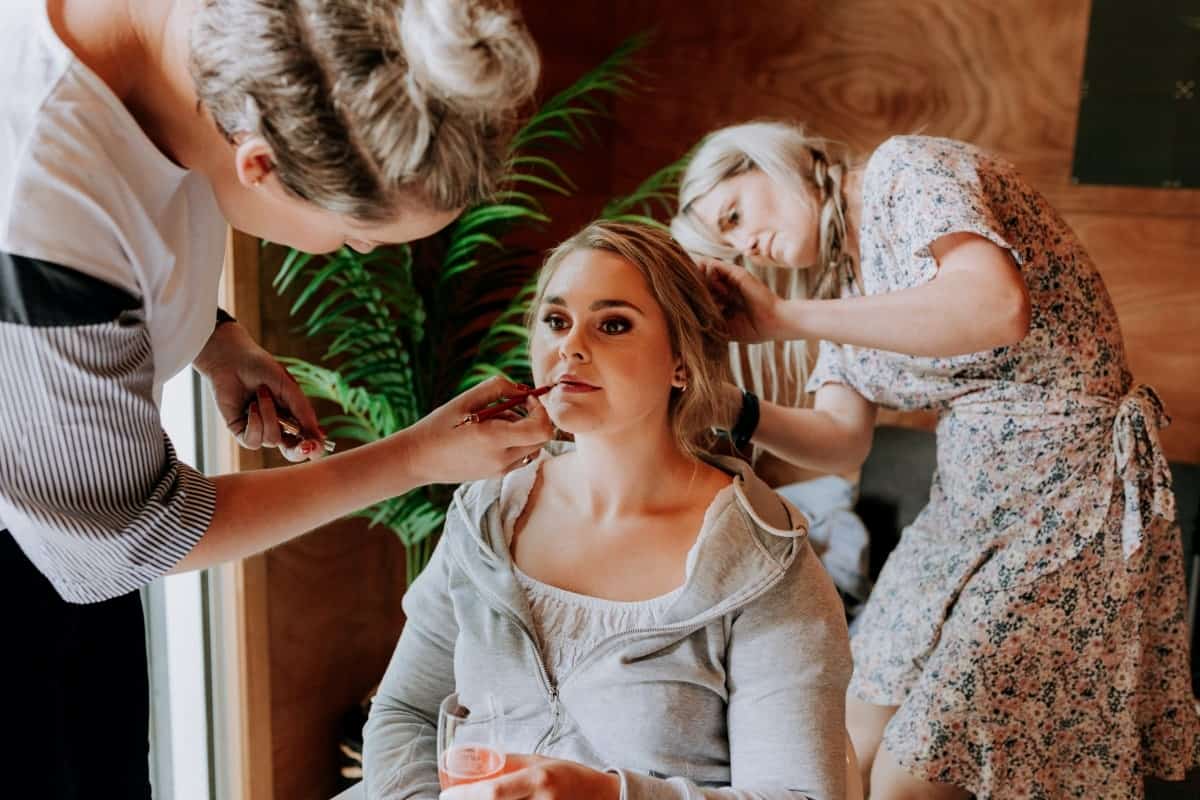 Makeup artist and assistant applying makeup on bride while sitting..