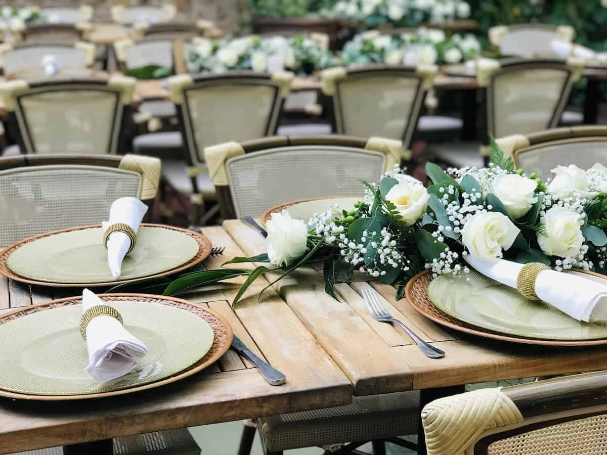 Wedding table decoration in Santo Domingo, Dominican Republic. Banquet. The chairs and wooden table for guests, served with cutlery, white roses flowers and crockery. Green and gold color pallet.