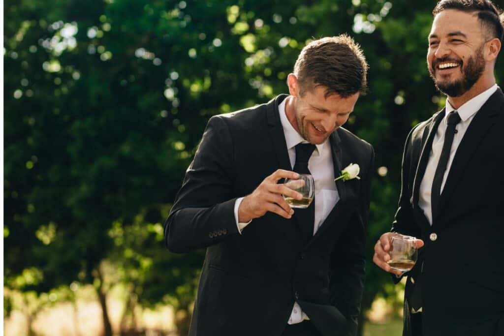 best man and groom laughing while holding a drink