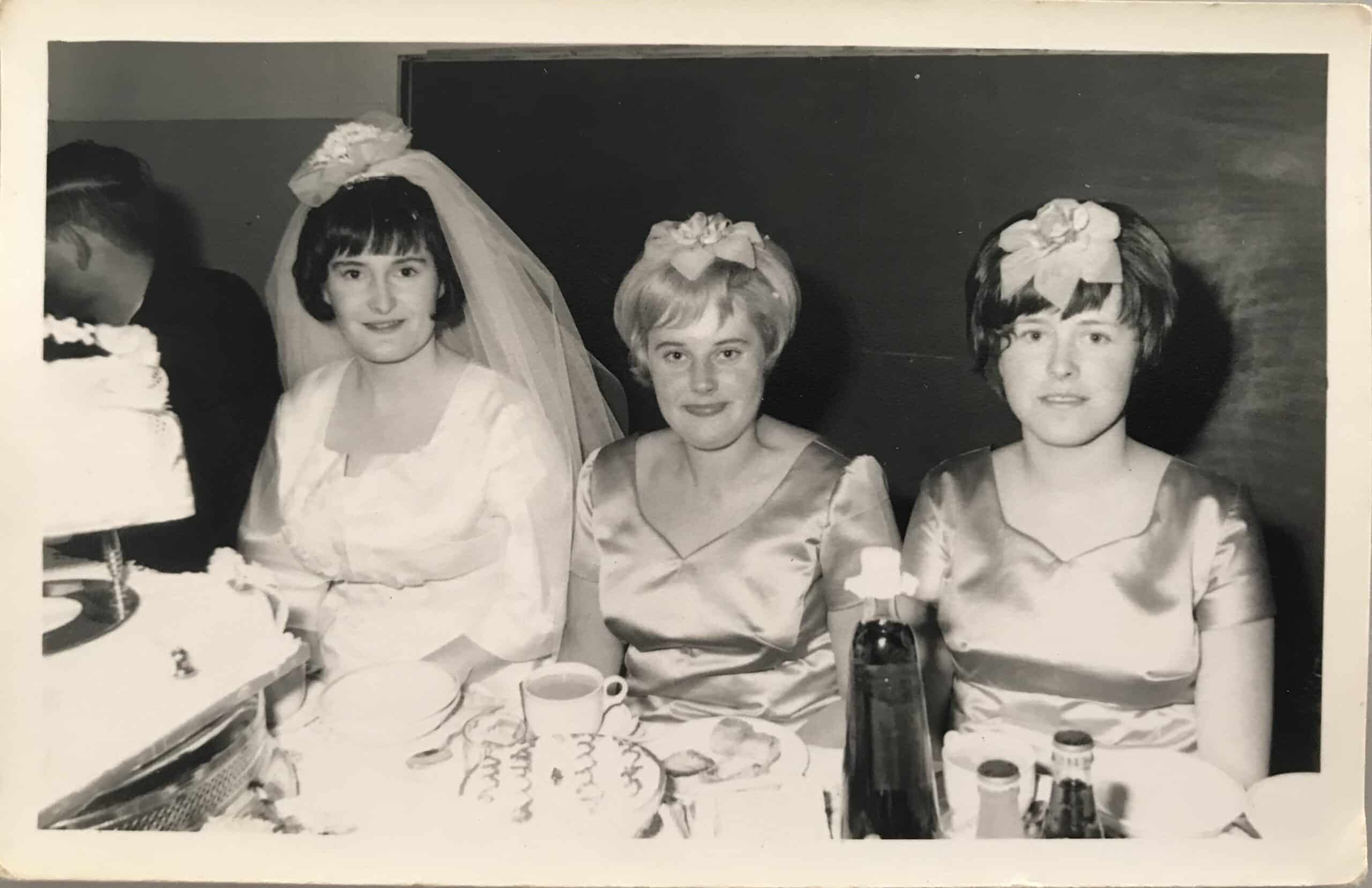 Bride seated with her bridesmaids at a table with wedding cake and dinner dishes on table